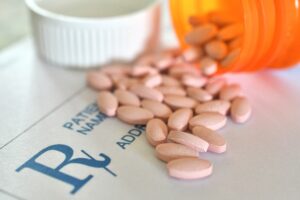 a bottle of pink oval pills spilling out over a prescription pad